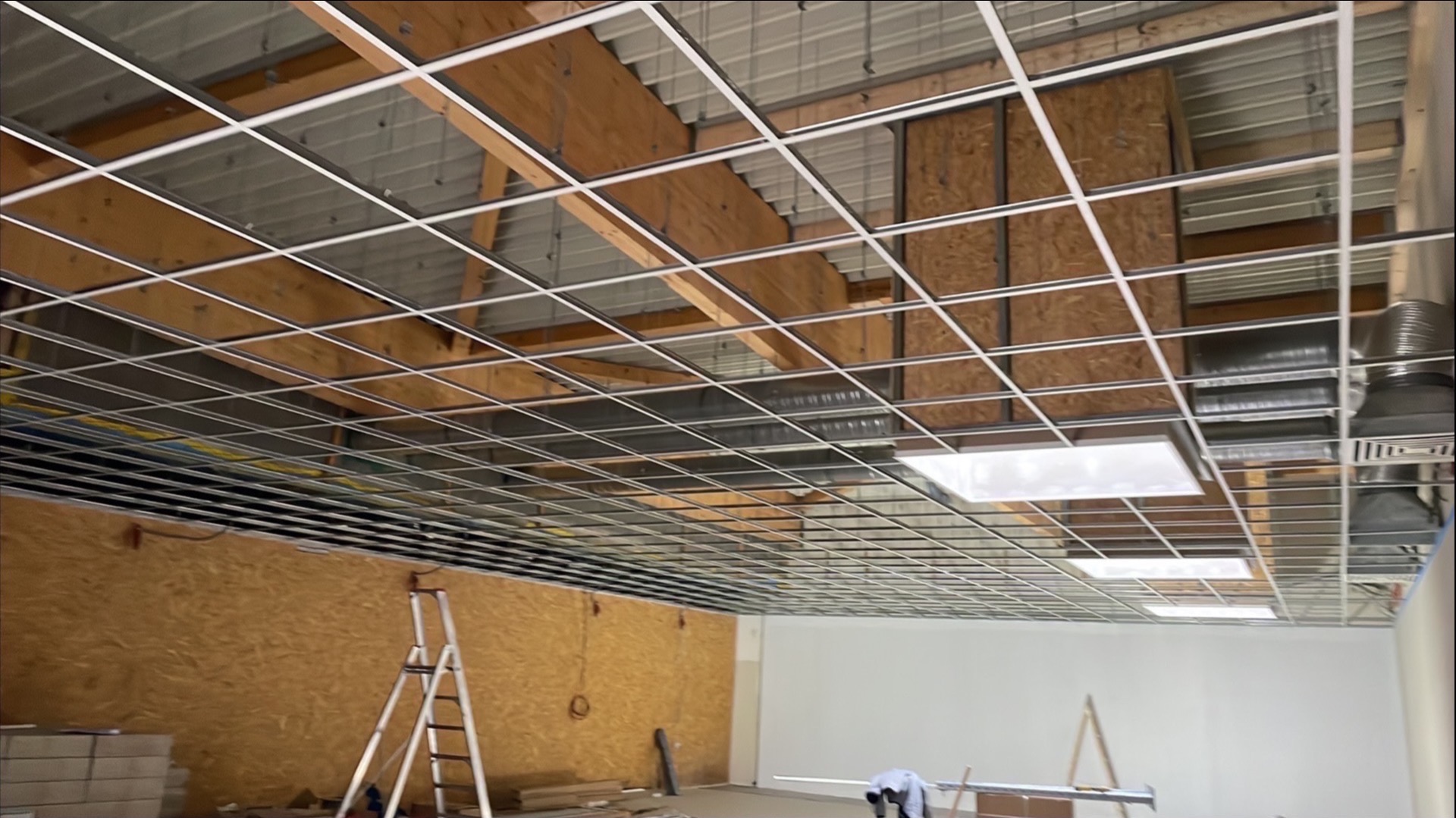 Montaż sufitu podwieszanego z widoczną konstrukcją metalową i oświetleniem w przestrzeni biurowej. Widoczna drabina i materiały budowlane.