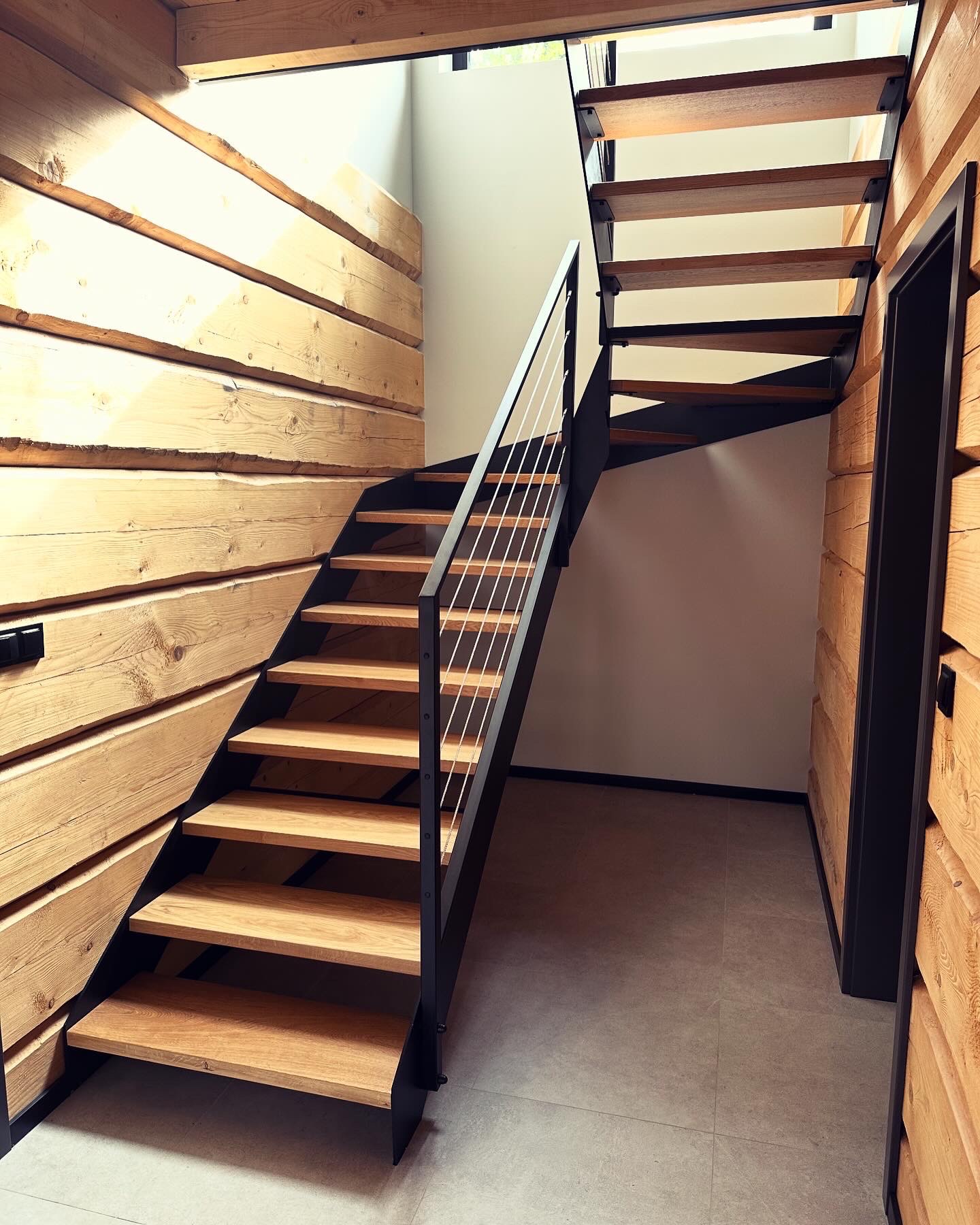 Nowoczesne schody z drewnianymi stopniami i metalową konstrukcją, wkomponowane w drewniane ściany. Minimalistyczny design i jasne oświetlenie.