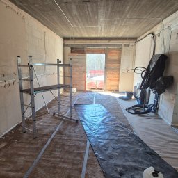 Wimar Usługi Remontowo Budowlane Marcin Kowalonek - Wnętrze w trakcie prac wykończeniowych: ściany z bloków, częściowo otynkowane, rozłożona folia ochronna, rusztowanie. Widoczne instalacje elektryczne.