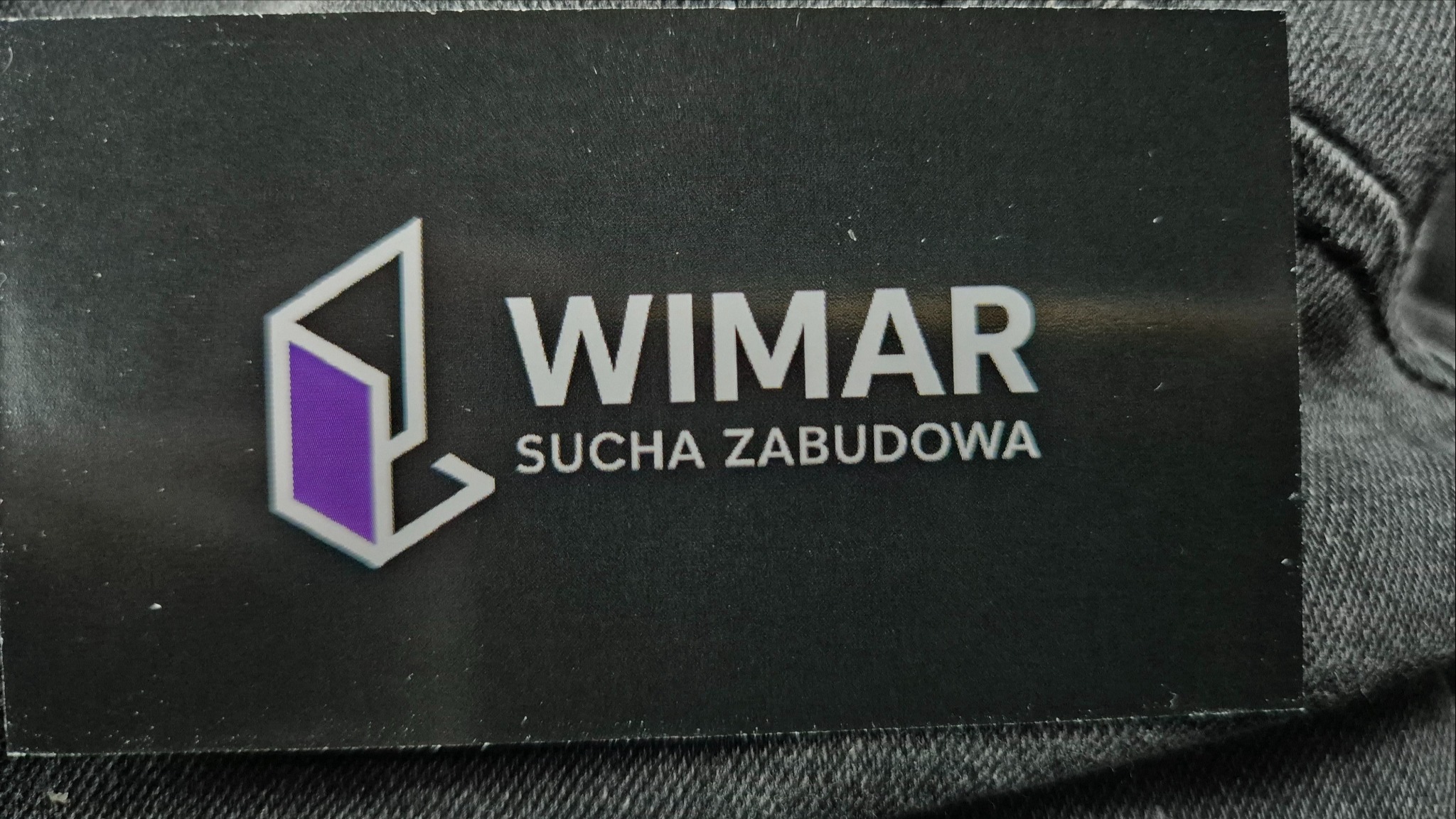 Wizytówka firmy Wimar. Logo z fioletowym akcentem i napis 'Sucha Zabudowa' na czarnym tle. Minimalistyczny design.