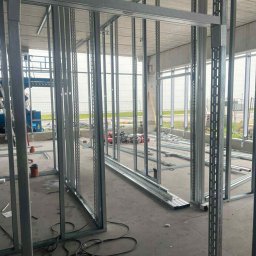 WMK INVESTMENT GROUP SPÓŁKA Z OGRANICZONĄ ODPOWIEDZIALNOŚCIĄ - Metalowa konstrukcja ścian działowych z profili, widok z bliska na surowy szkielet przed montażem płyt, narzędzia w tle, surowy beton na podłodze.