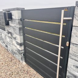 Daniel Zakrzewski Ogrodzenia - Nowoczesna brama wjazdowa z poziomymi panelami w kolorze grafitowym, z długim, pionowym uchwytem ze stali nierdzewnej. Brama osadzona na słupkach z szarego kamienia.