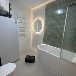 EDR - Nowoczesna łazienka z wanną, okrągłym lustrem z podświetleniem LED, grzejnikiem drabinkowym i czarną skrzynką narzędziową na podłodze.