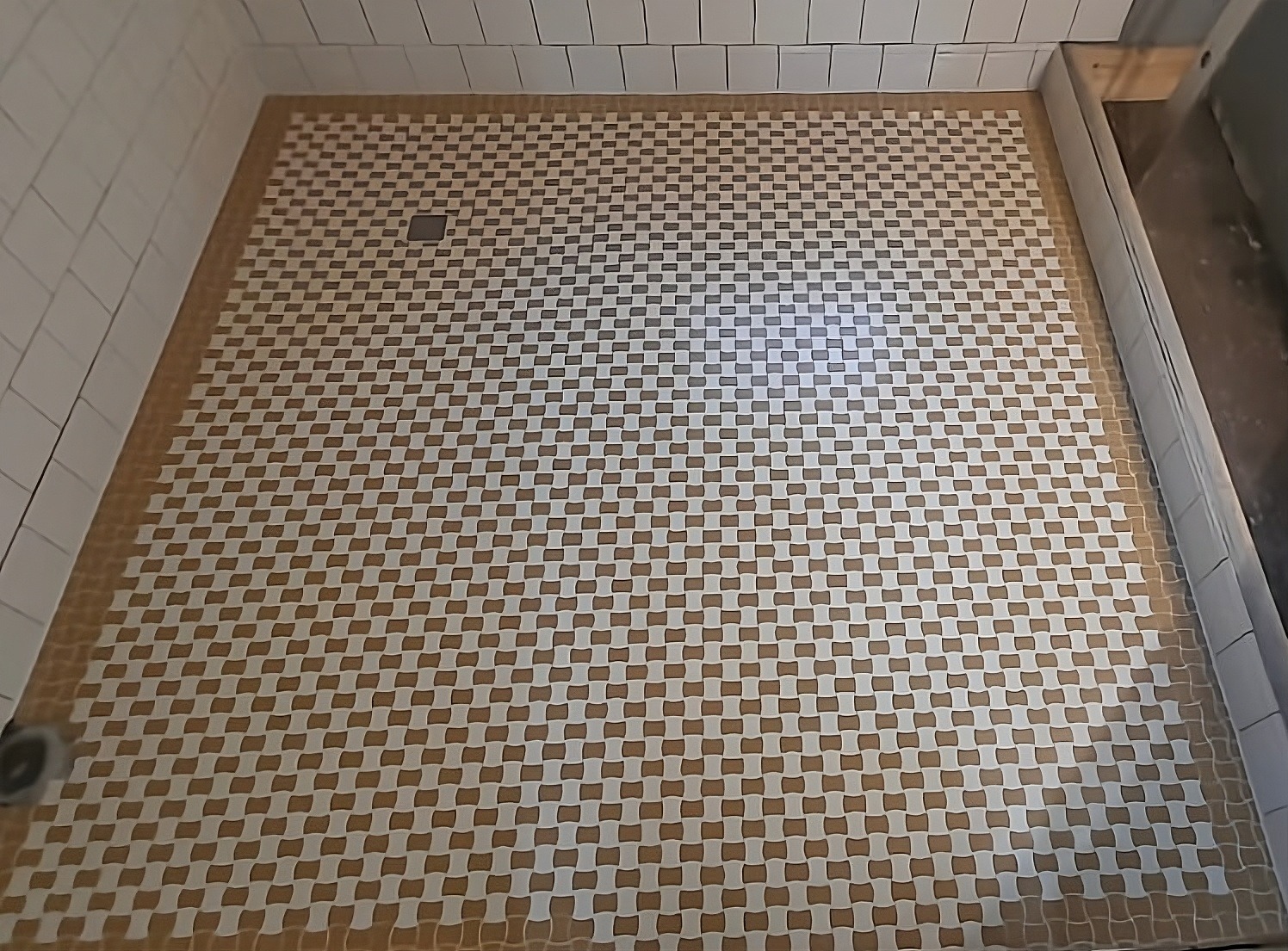 Ukończona podłoga prysznica z mozaiki w odcieniach bieli i brązu, widoczny odpływ liniowy i białe płytki ścienne, tworzące nowoczesny i estetyczny wygląd kabiny.