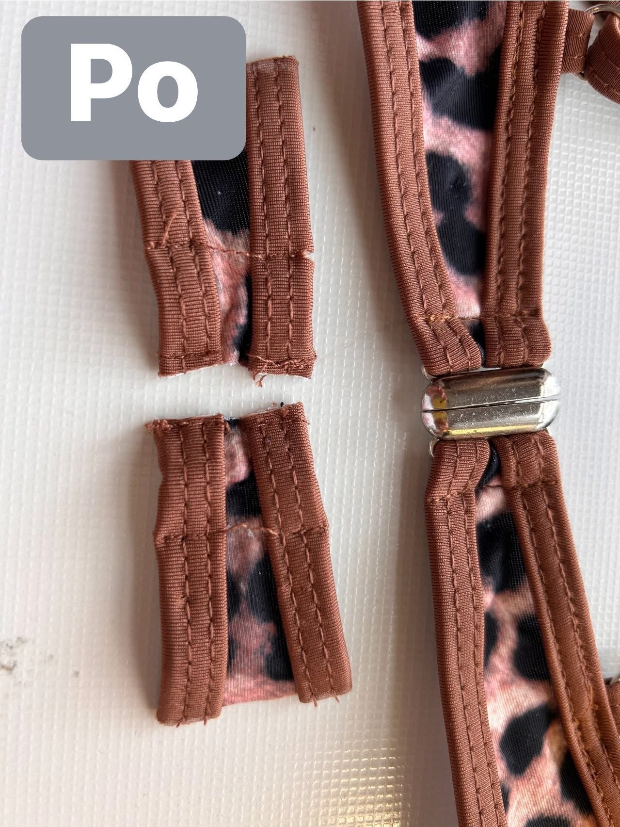 Fragment stroju kąpielowego z brązowym obszyciem w panterkę, z urwanym paskiem. Widoczny metalowy łącznik. Zdjęcie 'po' naprawie krawieckiej.