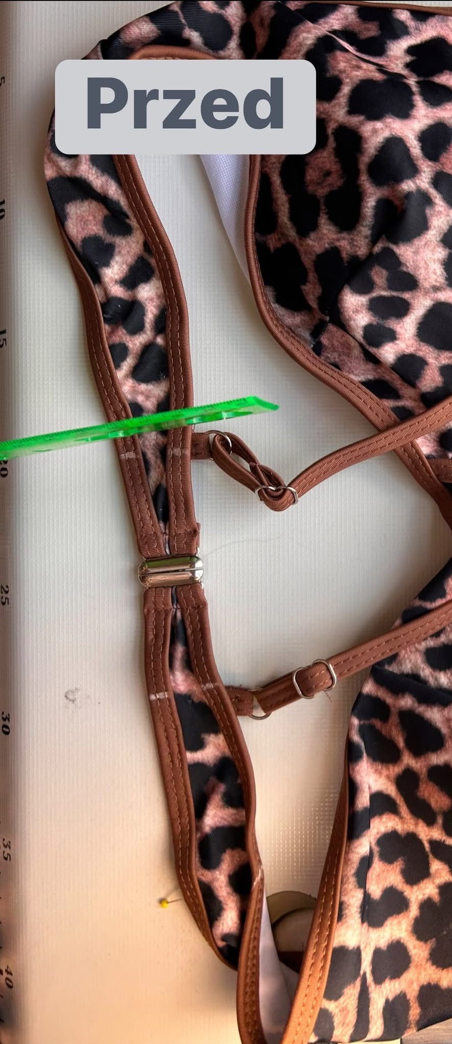 Fragment stroju kąpielowego w panterkę, z widoczną regulacją ramiączek i zieloną miarką. Ukazany etap pracy nad dopasowaniem, z użyciem szpilki.