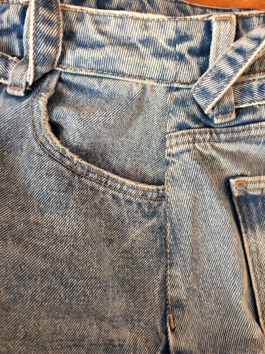 Fragment jasnych, spranych dżinsów z kieszenią i szlufkami, ukazujący detale szwów i fakturę denimu. Widoczne przeszycia i mocowania kieszeni.