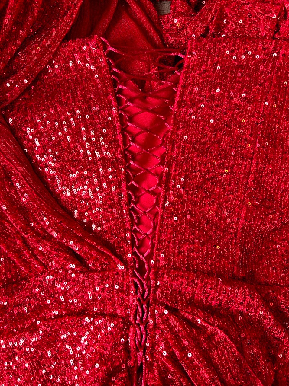 Czerwona, cekinowa suknia z wiązaniem na plecach, ukazana z bliska. Widoczne detale tkaniny i precyzyjne wykończenie. Elegancki krój i intensywny kolor.