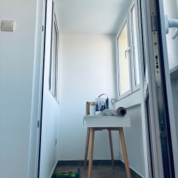 A&P Fach-Remont - Biały balkon po remoncie w Ścinawce Dolnej. Widoczne okna, białe ściany, stolik z farbami i narzędzia malarskie. Podłoga wyłożona płytkami.