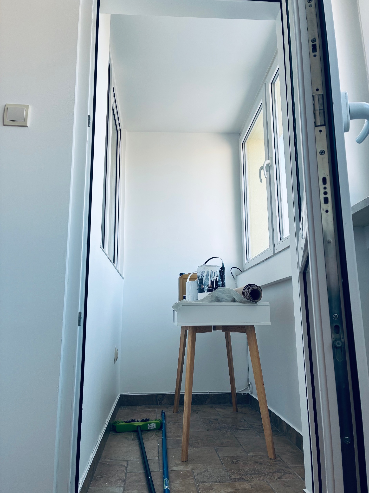 Biały balkon po remoncie w Ścinawce Dolnej. Widoczne okna, białe ściany, stolik z farbami i narzędzia malarskie. Podłoga wyłożona płytkami.