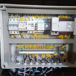 HTControl Hryhorii Tokarenko - Rozdzielnica elektryczna w szarej obudowie z widocznymi bezpiecznikami, przekaźnikami i przewodami oznaczonymi żółtymi tulejkami. Widoczne elementy sterowania i zasilania.