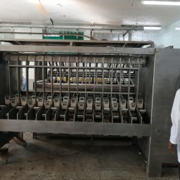 HTControl Hryhorii Tokarenko - Metalowa konstrukcja z rzędami uchwytów w hali produkcyjnej, widoczna osoba w białym fartuchu i kapeluszu. Oświetlenie jarzeniowe, płytki na ścianach.