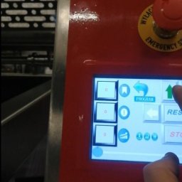 HTControl Hryhorii Tokarenko - Panel sterowania maszyny przemysłowej z dotykowym ekranem i przyciskiem awaryjnym, obsługiwany przez osobę. Widoczne ikony i napisy na ekranie.