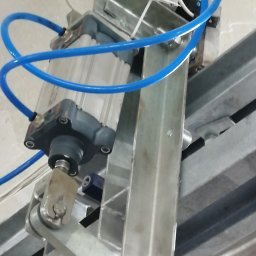 HTControl Hryhorii Tokarenko - Szczegółowe ujęcie siłownika pneumatycznego z niebieskimi przewodami, zamontowanego na metalowej konstrukcji. Widoczne elementy mocujące i fragment sufitu w tle.