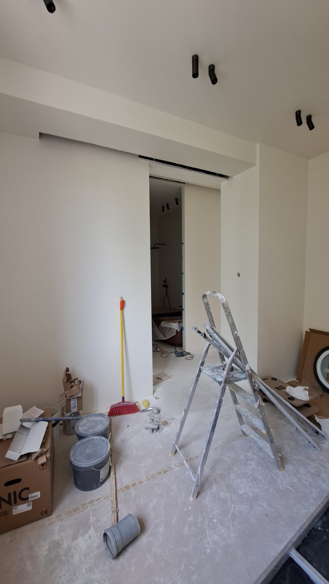 Wnętrze w trakcie prac wykończeniowych w Grodzisku Mazowieckim. Widoczne ściany po nałożeniu gładzi, drabina malarska i akcesoria malarskie. W tle widoczna łazienka.