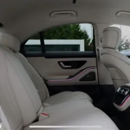 Luksusowe wnętrze samochodu z jasną skórzaną tapicerką, podświetleniem ambientowym i widokiem na zewnątrz przez okno.