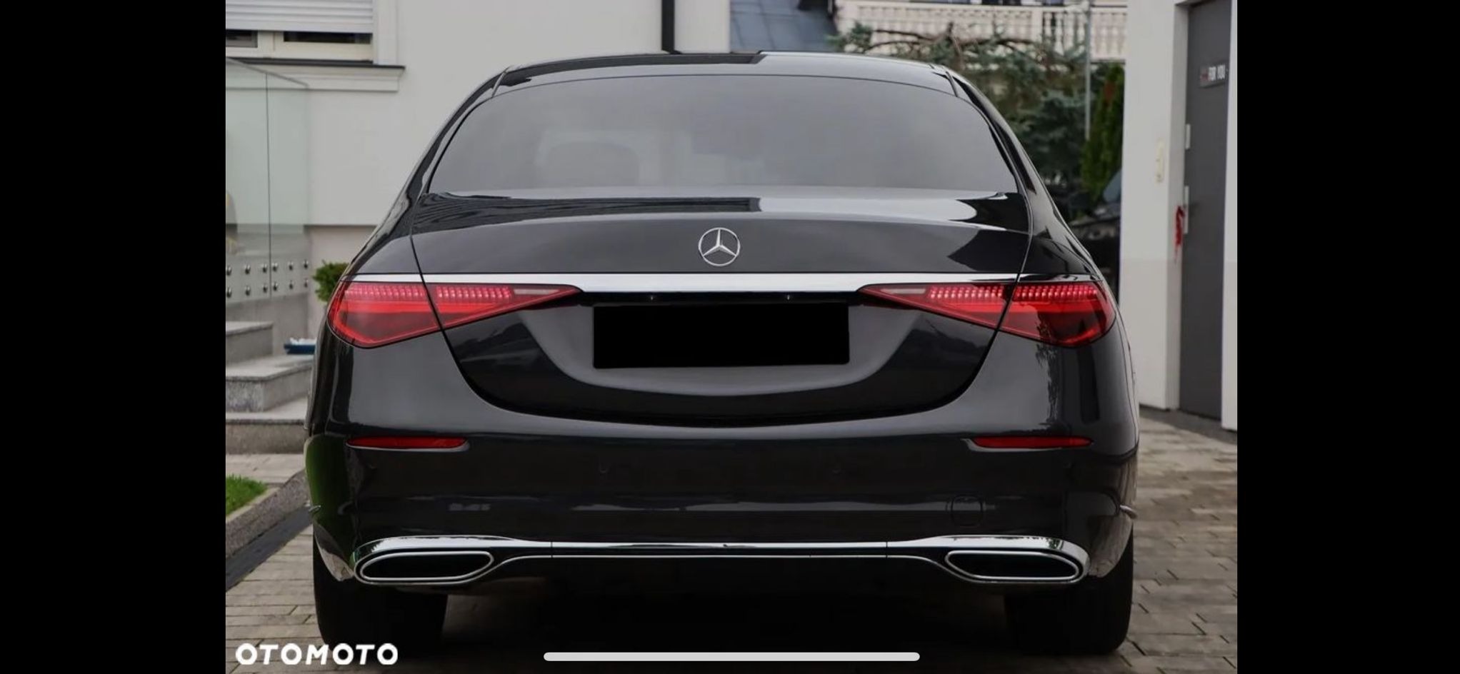 Elegancki, czarny Mercedes klasy S z chromowanymi detalami, widziany z tyłu na tle nowoczesnego budynku. Widoczne światła LED i logo marki.