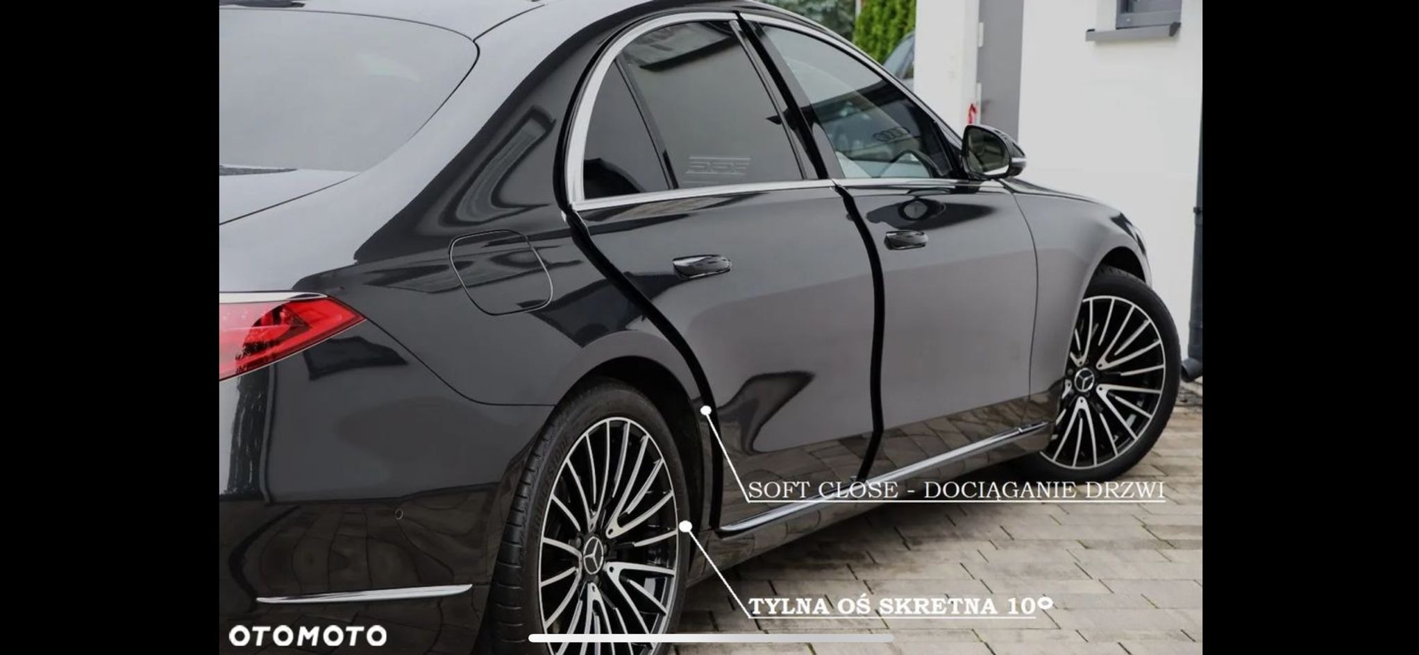 Czarny, luksusowy sedan z otwartymi drzwiami, ukazujący system dociągania. Widoczna tylna oś skrętna. Prezentacja nowoczesnych rozwiązań w samochodzie.