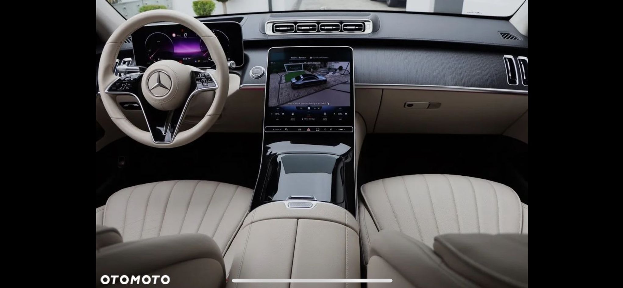 Wnętrze luksusowego samochodu marki Mercedes z beżową skórzaną tapicerką i nowoczesnym systemem multimedialnym z widokiem z kamery 360 stopni.