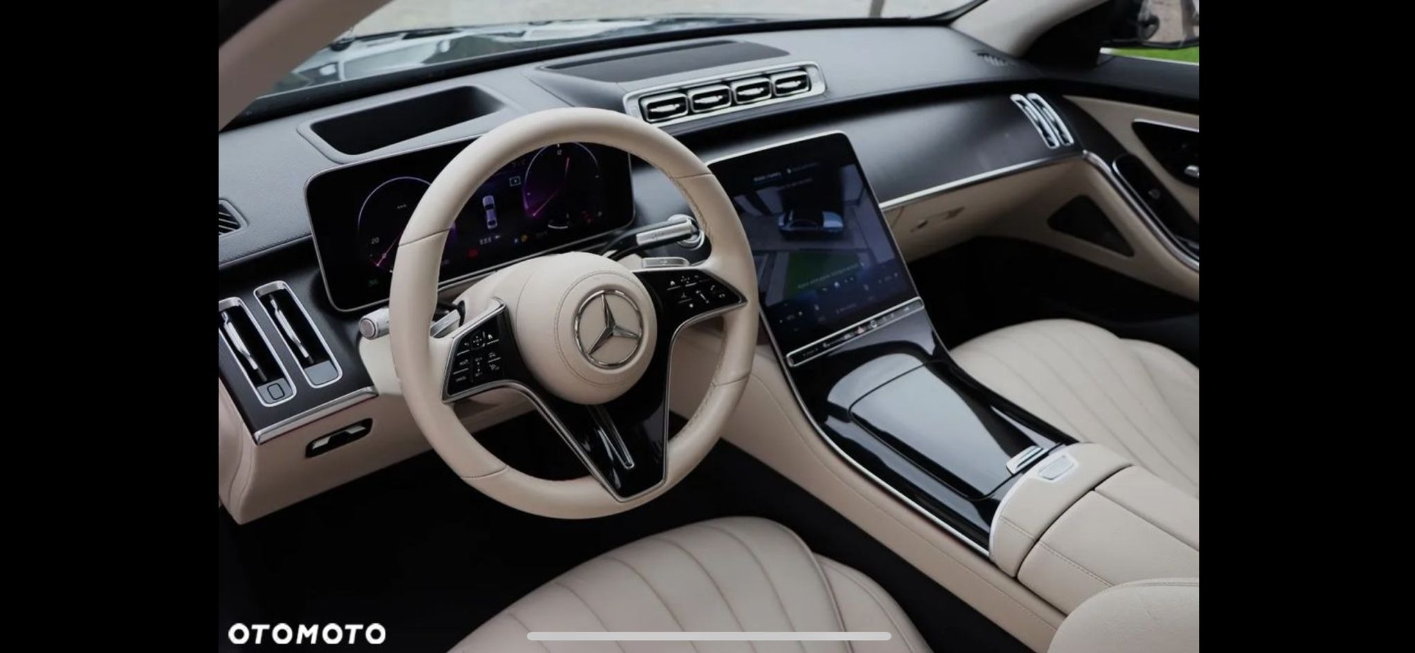 Wnętrze luksusowego samochodu Mercedes-Benz z beżową skórzaną tapicerką, widok na deskę rozdzielczą, kierownicę i centralny wyświetlacz. Elegancki design.