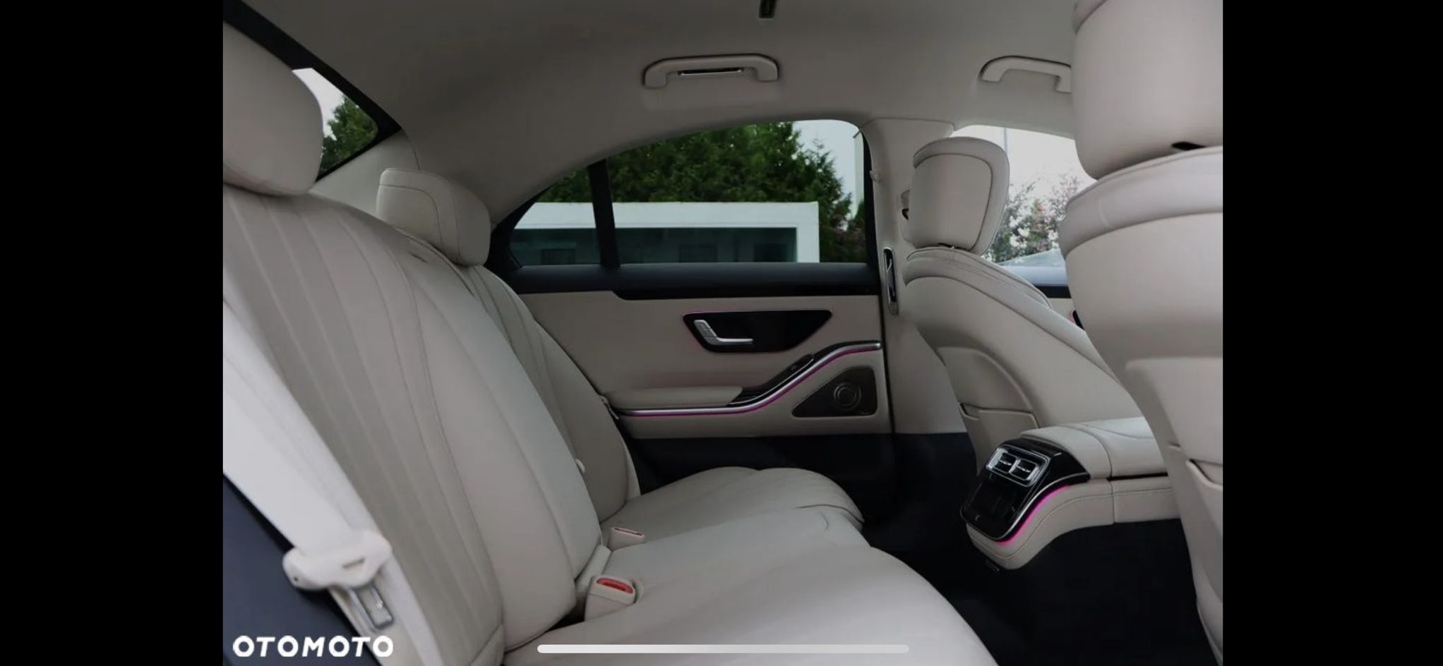 Luksusowe wnętrze samochodu z jasną skórzaną tapicerką, podświetleniem ambientowym i widokiem na zewnątrz przez okno.