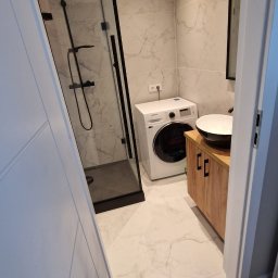 SZBF - Nowoczesna łazienka z kabiną prysznicową typu walk-in, pralką i umywalką nablatową na szafce z drewnianymi frontami. Marmurowe płytki na ścianach i podłodze.