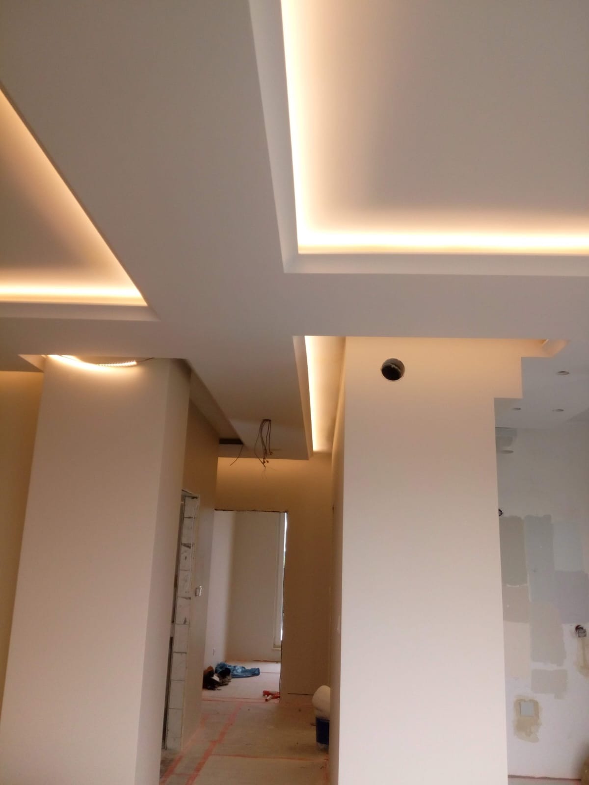 Nowoczesny sufit podwieszany z oświetleniem LED. Białe ściany w pomieszczeniu w trakcie remontu. Widok z dołu, perspektywa wnętrza.