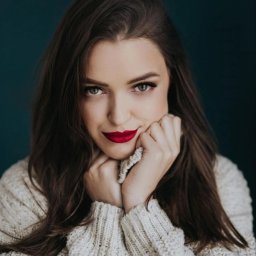 Przedsiębiorstwo Handlowo-Usługowe DAWID KREPS - Portret kobiety z długimi brązowymi włosami, w kremowym swetrze, z czerwonymi ustami na ciemnym tle. Dłonie pod brodą, spojrzenie w obiektyw.