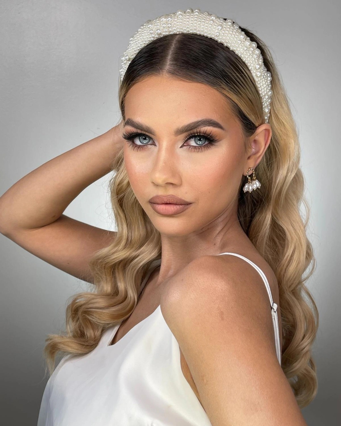 Portret kobiety z blond włosami, w białej sukience i perłowej opasce, prezentującej profesjonalny makijaż z wyraźnie podkreślonymi oczami i ustami.