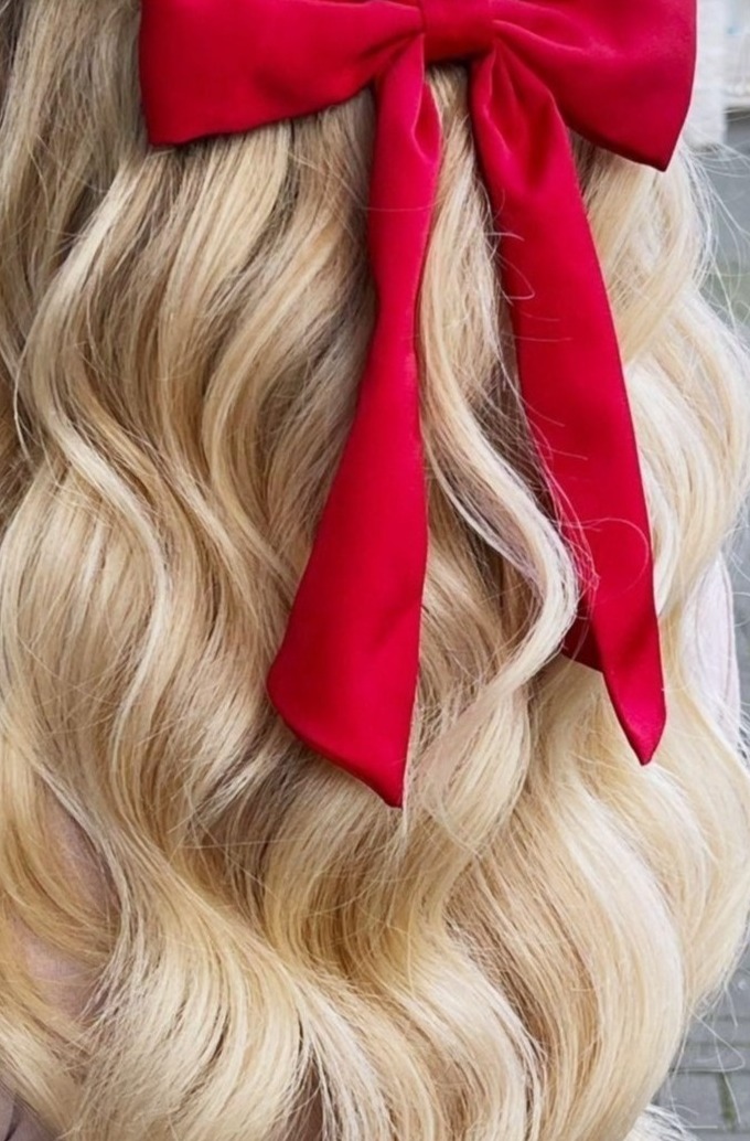 Blond włosy z delikatnymi falami, upięte czerwoną, satynową kokardą. Widok z bliska, skupiony na fryzurze i dodatku.