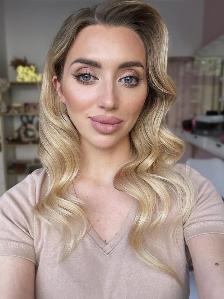 Portret kobiety z profesjonalnym makijażem i blond włosami ułożonymi w fale. Delikatny makijaż oczu i ust w odcieniach nude. Subtelne oświetlenie podkreśla rysy twarzy.