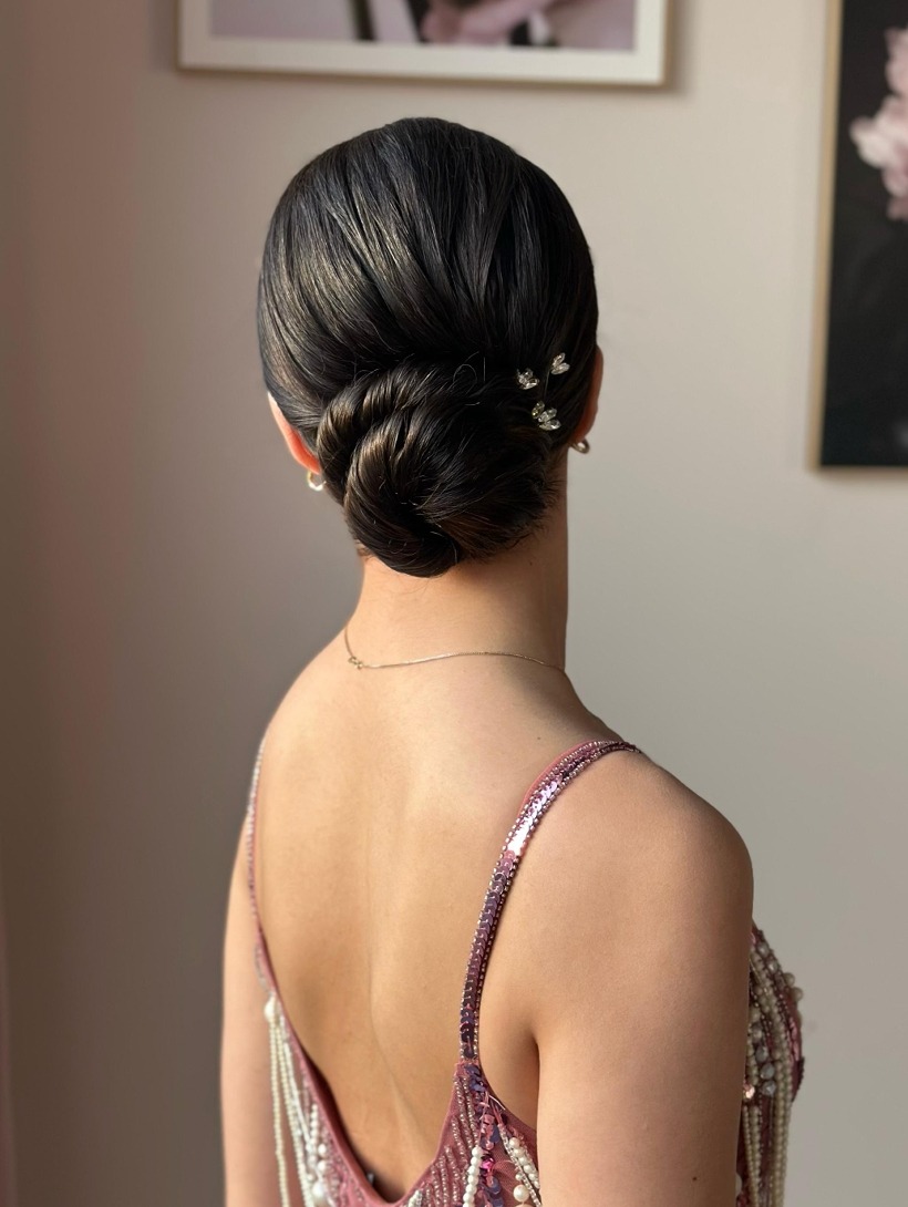 Elegancka fryzura upięta w kok z ozdobnymi wsuwkami, widok z tyłu, podkreślona sukienka z cekinami i perłami, subtelny łańcuszek na szyi, delikatne kolczyki.