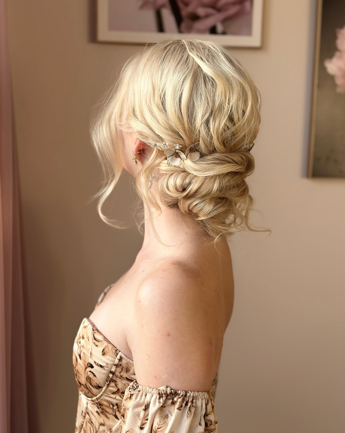 Eleganckie upięcie blond włosów z ozdobną spinką, widok z profilu. Delikatny makijaż i sukienka z motywem roślinnym dopełniają stylizację.