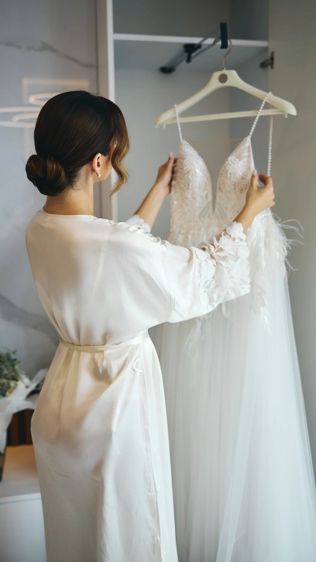 Panna młoda w szlafroku ogląda suknię ślubną z koronkowymi aplikacjami i piórami w Tychach. Przygotowania do ceremonii, elegancka garderoba.