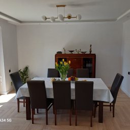 FIRMA REMONTOWA FINISZ SIKORA WIESŁAW - Jasne wnętrze jadalni z parkietem ułożonym w jodełkę, białymi ścianami, listwami przysufitowymi i złotym żyrandolem nad stołem z bukietem tulipanów.