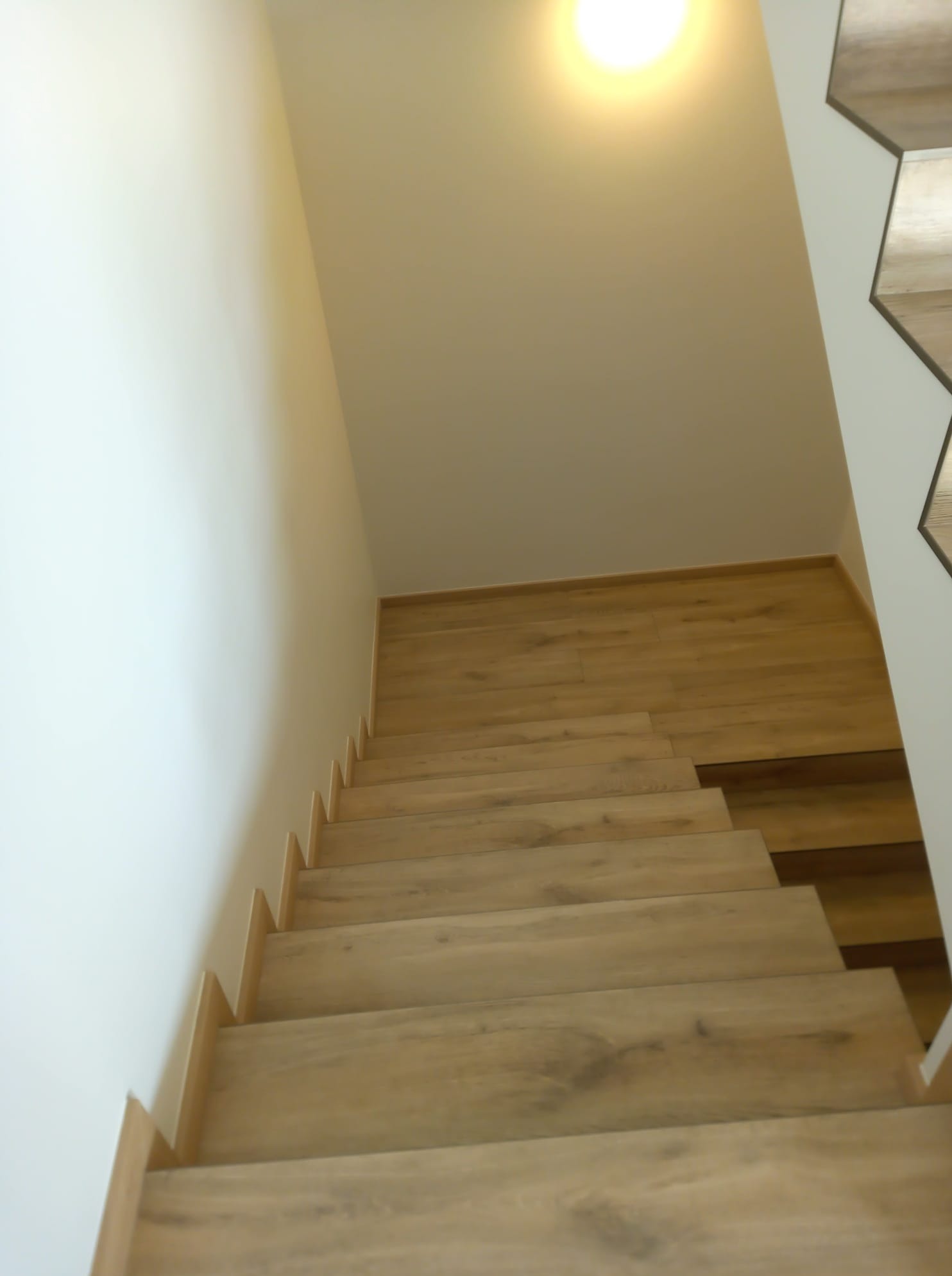 Nowoczesne schody z drewnianymi stopniami, oświetlone od góry, z fragmentem dekoracyjnej ściany z heksagonów po prawej stronie.