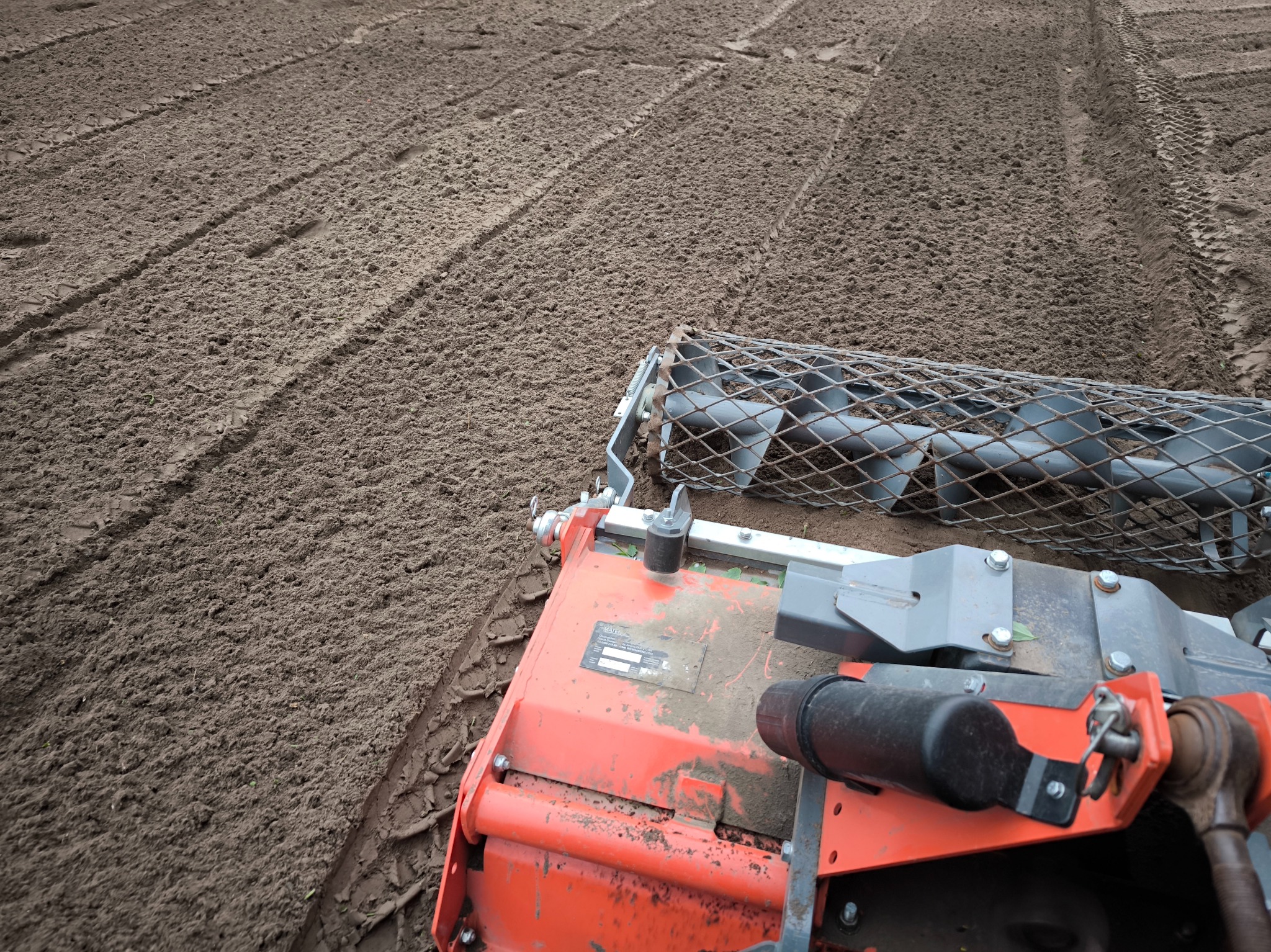 Przygotowanie gleby pod trawnik: glebogryzarka spulchnia ziemię, pozostawiając równe bruzdy. Widok z góry na maszynę i świeżo obrobioną ziemię.