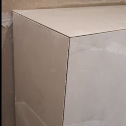 Dariusz Piwoński - Wykończony fragment obudowy z płytek imitujących marmur, z widocznymi fugami i surową ścianą w tle, prezentujący precyzję wykonania.