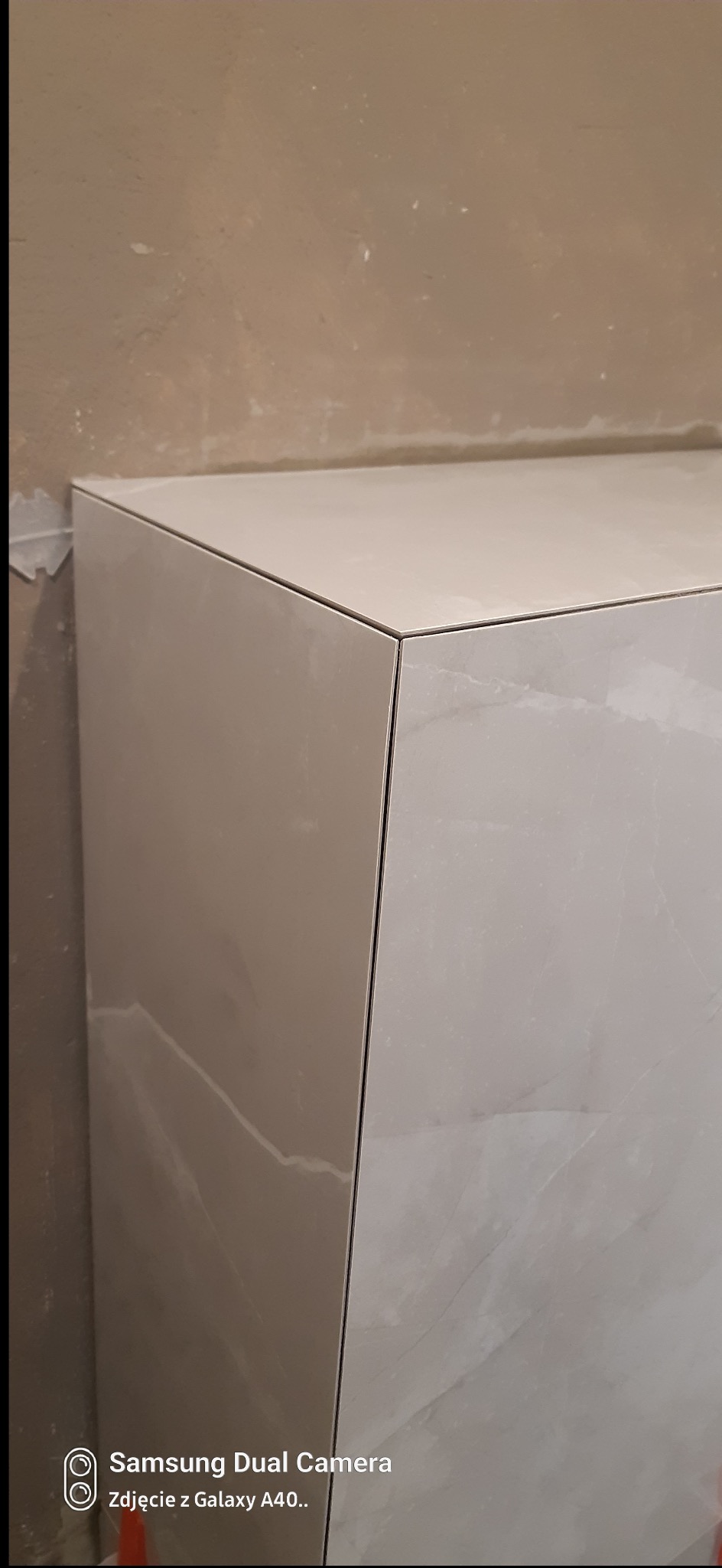 Wykończony fragment obudowy z płytek imitujących marmur, z widocznymi fugami i surową ścianą w tle, prezentujący precyzję wykonania.