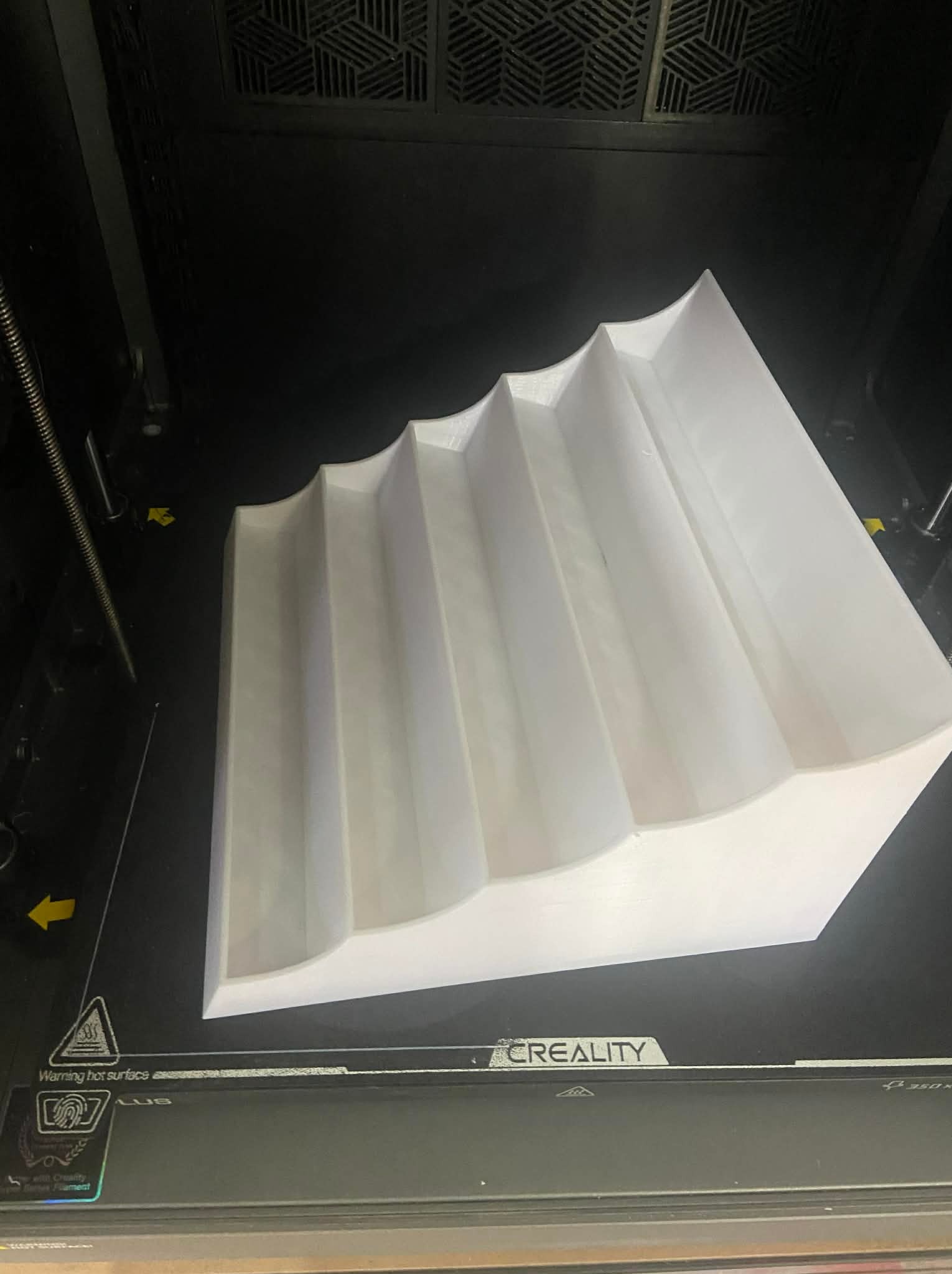 Biały, falisty element wydrukowany w 3D, leżący na platformie drukarki Creality. Widoczne ostrzeżenie o gorącej powierzchni i oznaczenia drukarki.