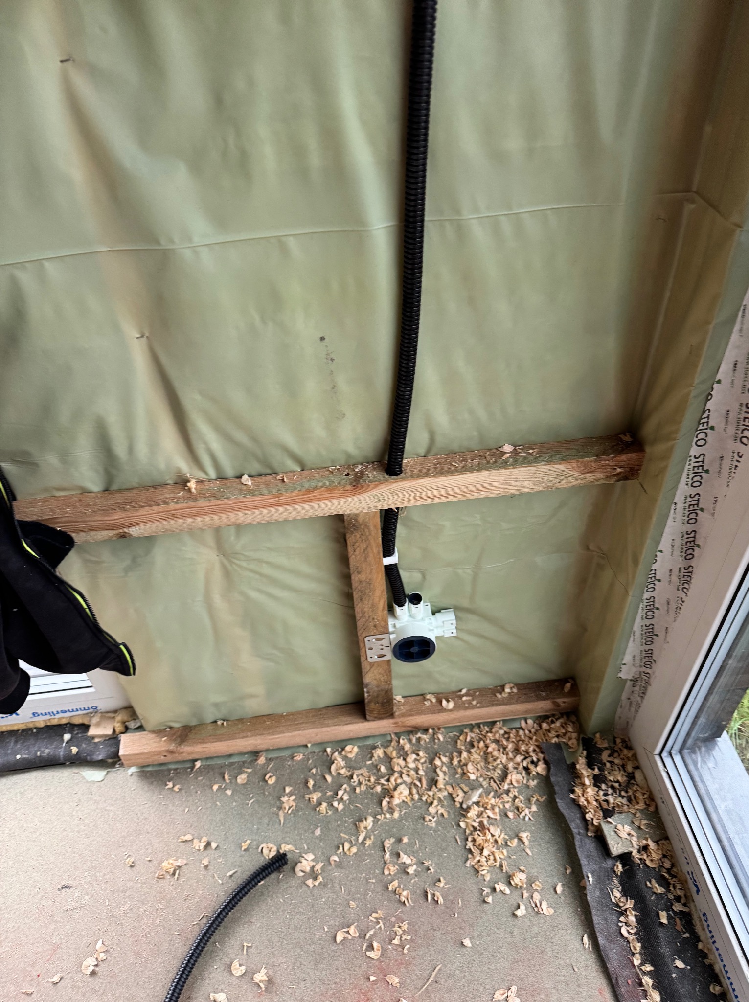 Wnętrze w trakcie budowy: drewniane belki, folia izolacyjna i instalacja elektryczna z peszlem. Wióry na podłodze. Widoczne okno.