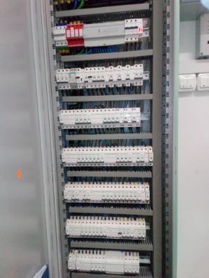 Rozdzielnica elektryczna z zabezpieczeniami różnicowoprądowymi i ogranicznikami przepięć, widok z bliska na zainstalowane komponenty w szarej szafie.