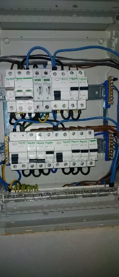Rozdzielnia elektryczna z zamontowanymi bezpiecznikami Schneider Electric i okablowaniem w kolorach niebieskim, brązowym i żółto-zielonym.