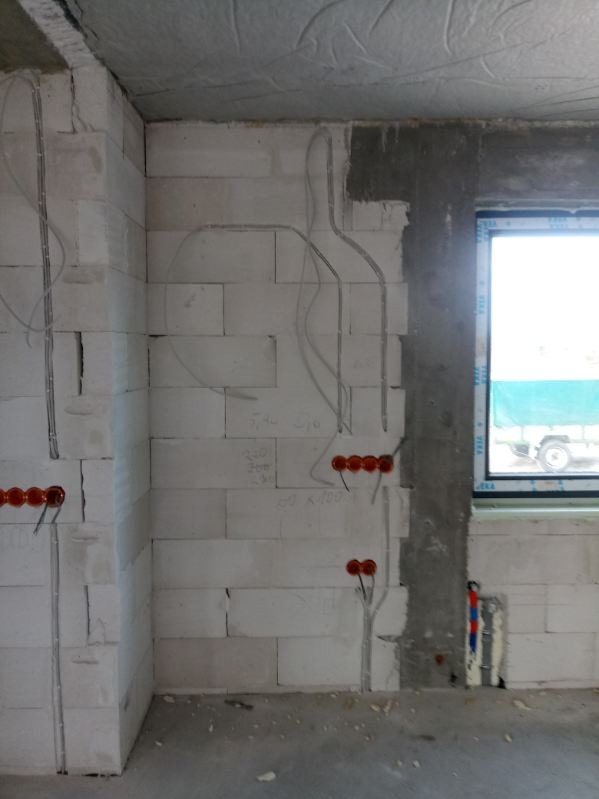 Surowe ściany z betonu komórkowego z bruzdami na kable elektryczne i puszkami instalacyjnymi. Widoczne przewody i notatki na ścianie. Stan surowy instalacji elektrycznej.