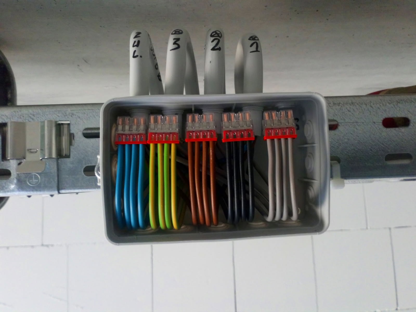 Rozdzielnica elektryczna z podłączonymi przewodami o różnych kolorach, przymocowana do metalowej szyny montażowej, widok z dołu.