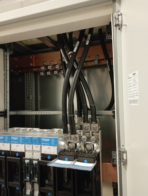 Rozdzielnica elektryczna Hager z podłączonymi przewodami oznaczonymi etykietami, widoczne bezpieczniki. Detal instalacji wewnątrz szafy.