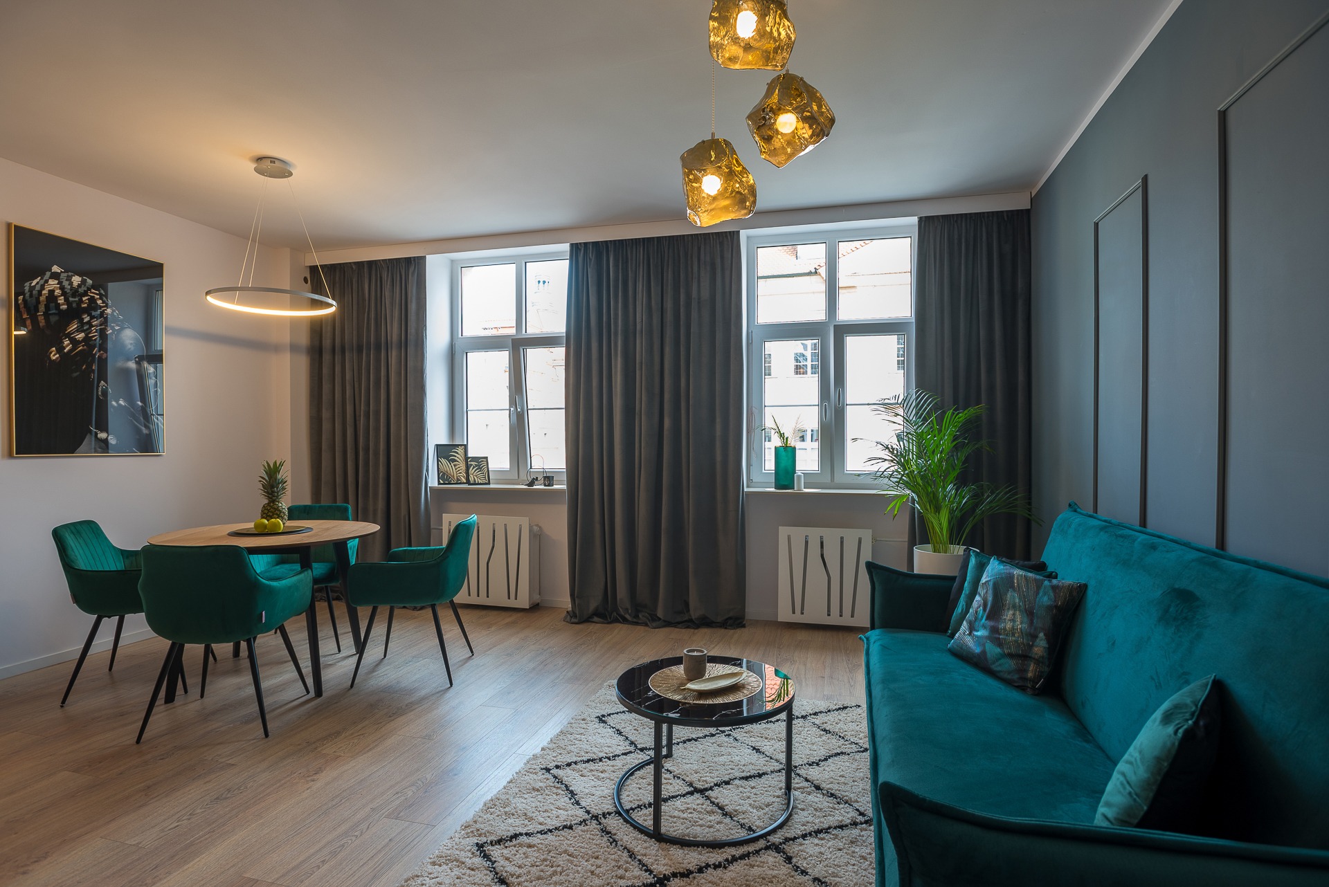 Turkusowe meble w jasnym salonie z drewnianą podłogą, okrągłym stołem i lampami w stylu glamour. Nowoczesne wnętrze z roślinami i dekoracjami.