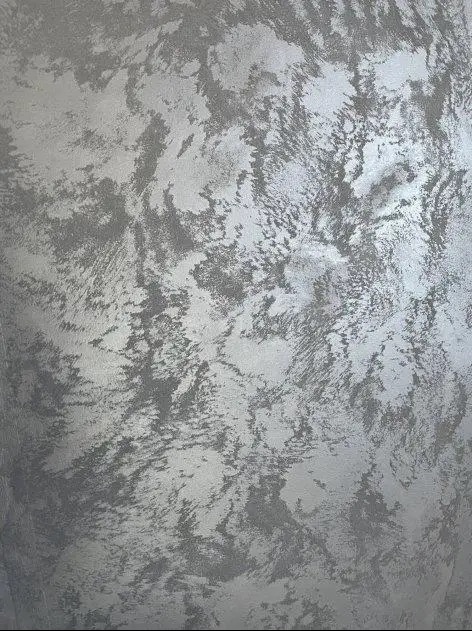 Srebrzysta ściana z dekoracyjną fakturą, imitującą chmurę lub marmurkową powierzchnię. Wykończenie z efektem połysku, widoczne nieregularne wzory i cieniowania.