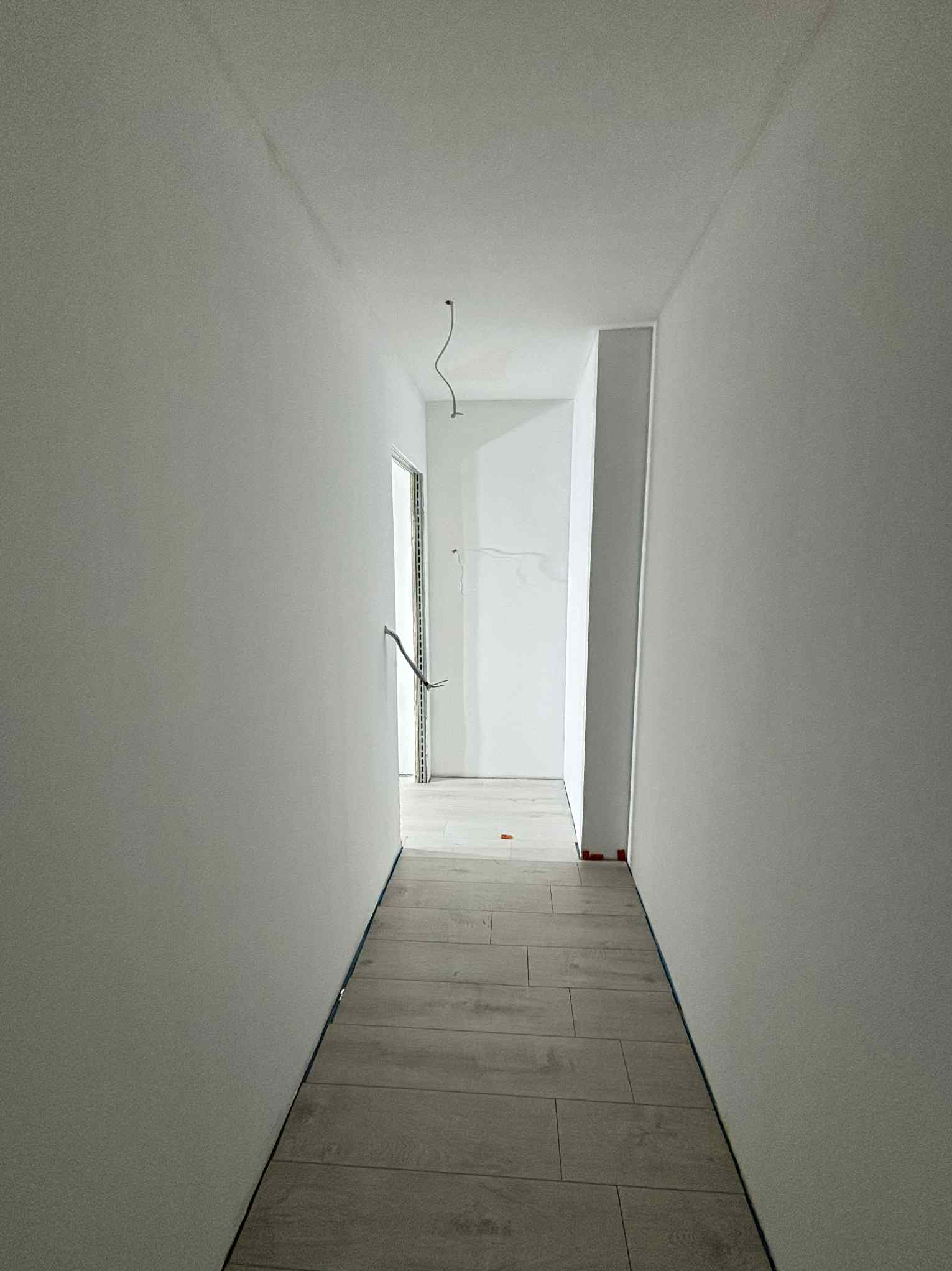 Jasny korytarz po remoncie: świeżo położone panele podłogowe, gładkie, pomalowane na biało ściany. Widoczne wystające kable i listwy przypodłogowe.