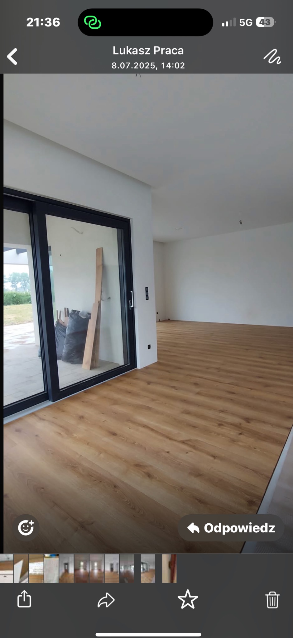 Jasna podłoga z paneli ułożona w przestronnym wnętrzu z dużym przesuwnym oknem. Widoczne materiały budowlane sugerują etap wykończeniowy.